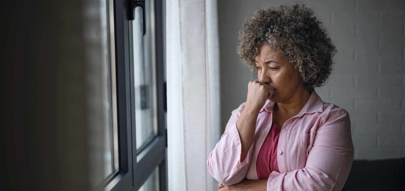 Woman looking thoughtfully out window, appearing tired and contemplative.